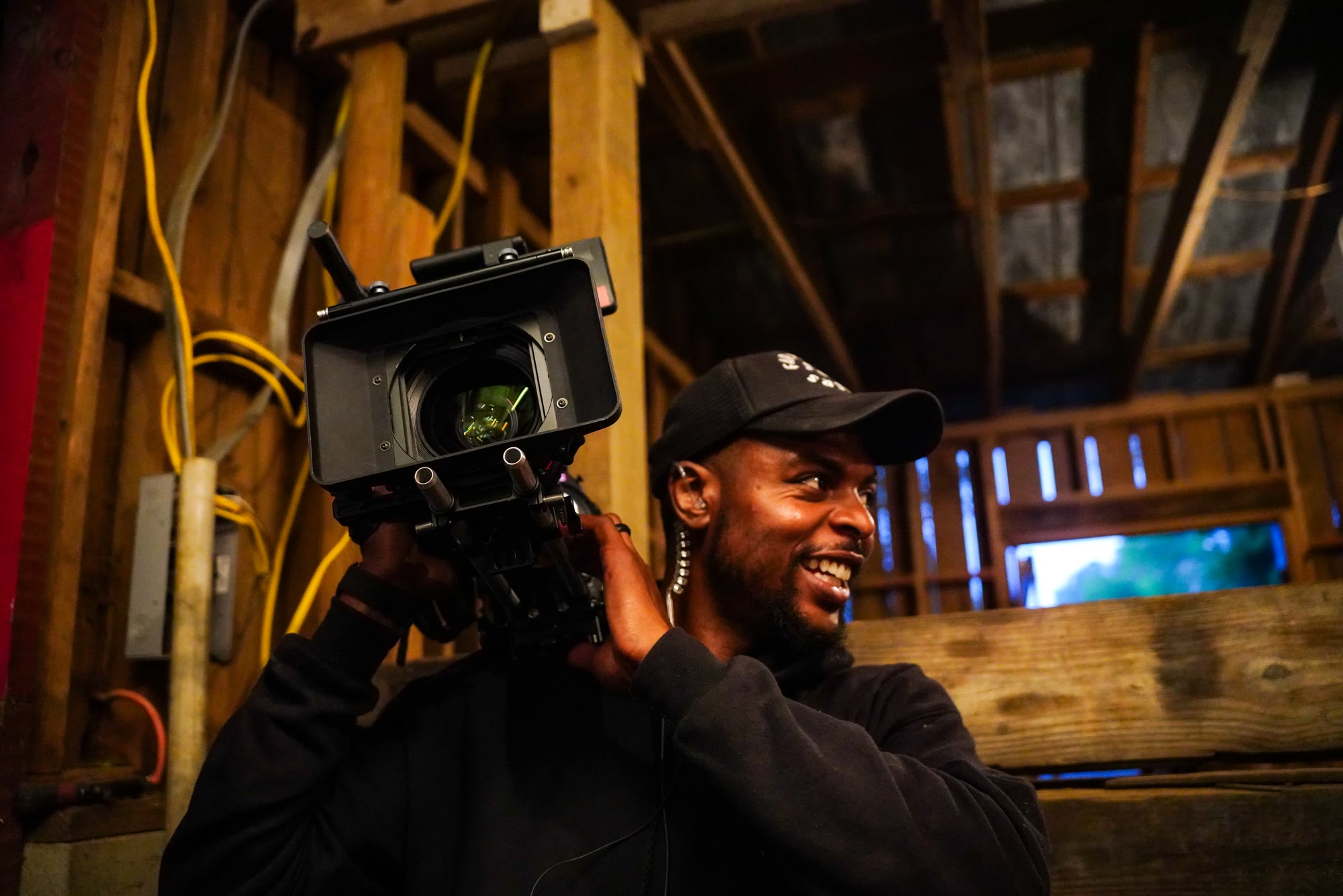 Tondric smiling behind a cinema camera on location in a rustic barn