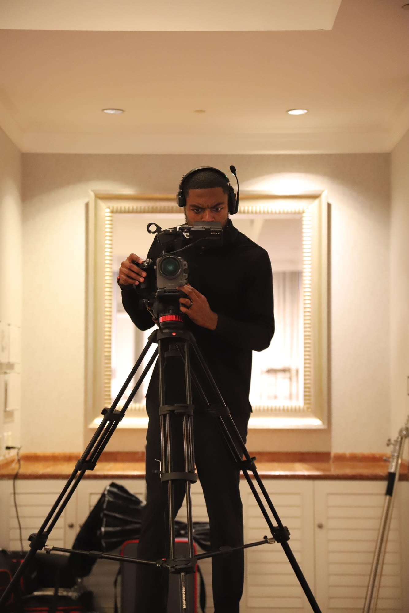 Tondric on headset behind a camera on a tripod at an indoor event